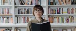 Image d'une femme tenant un livre devant une bibliothèque.