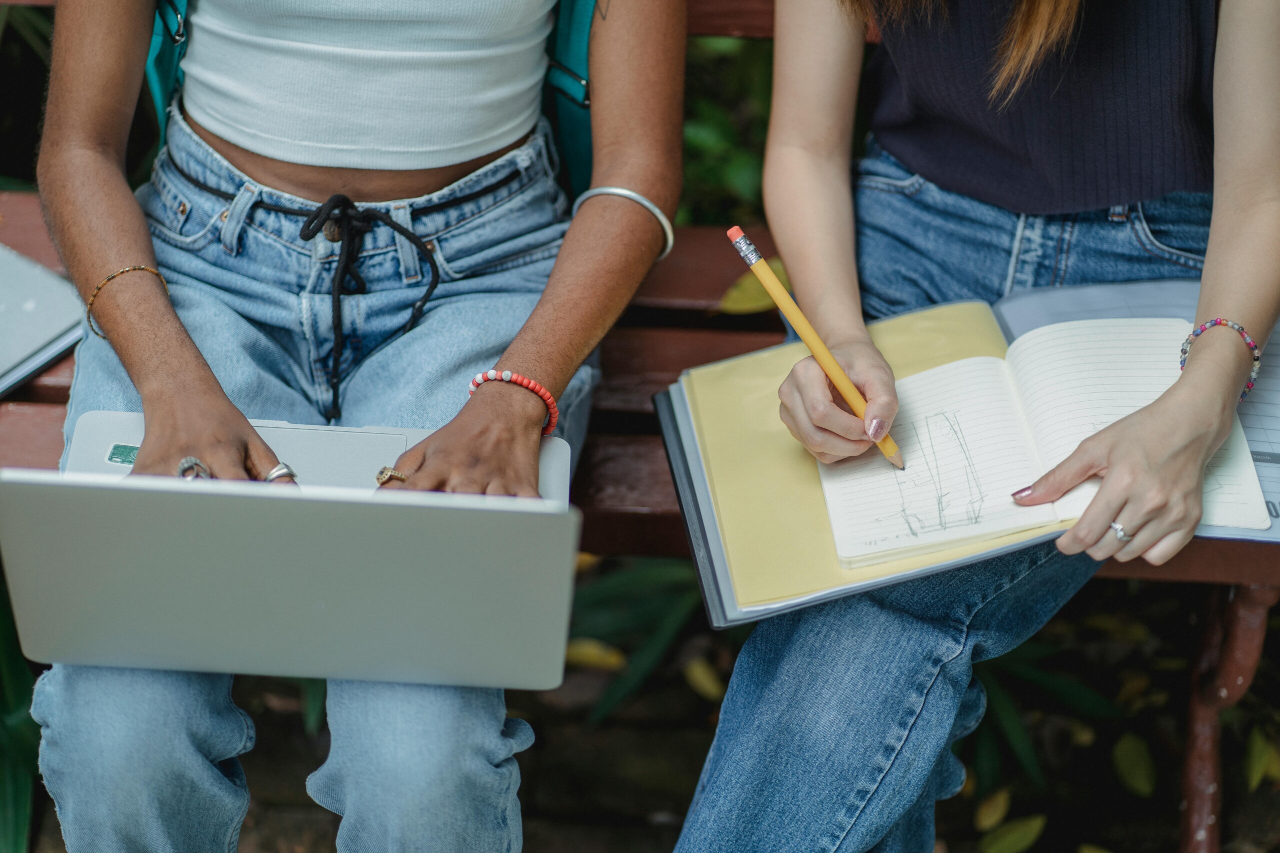 Photo d'une étudiante tenant un ordinateur sur ses genoux à côté d'une étudiante prenant des notes sur ses genoux.