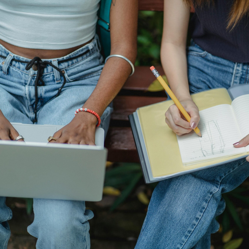 Photo d'une étudiante tenant un ordinateur sur ses genoux à côté d'une étudiante prenant des notes sur ses genoux.